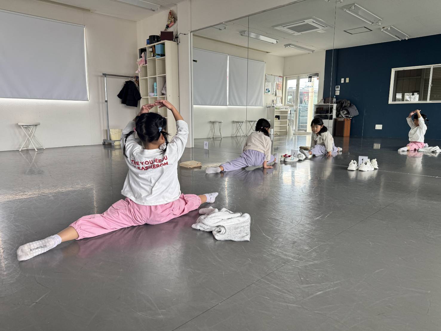 壁一面の鏡があるスタジオで、開脚ストレッチをする女の子